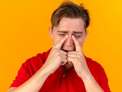 close-up-view-sad-young-handsome-blonde-ill-man-touching-nose-with-closed-eyes-isolated-orange-wall-(1).webp